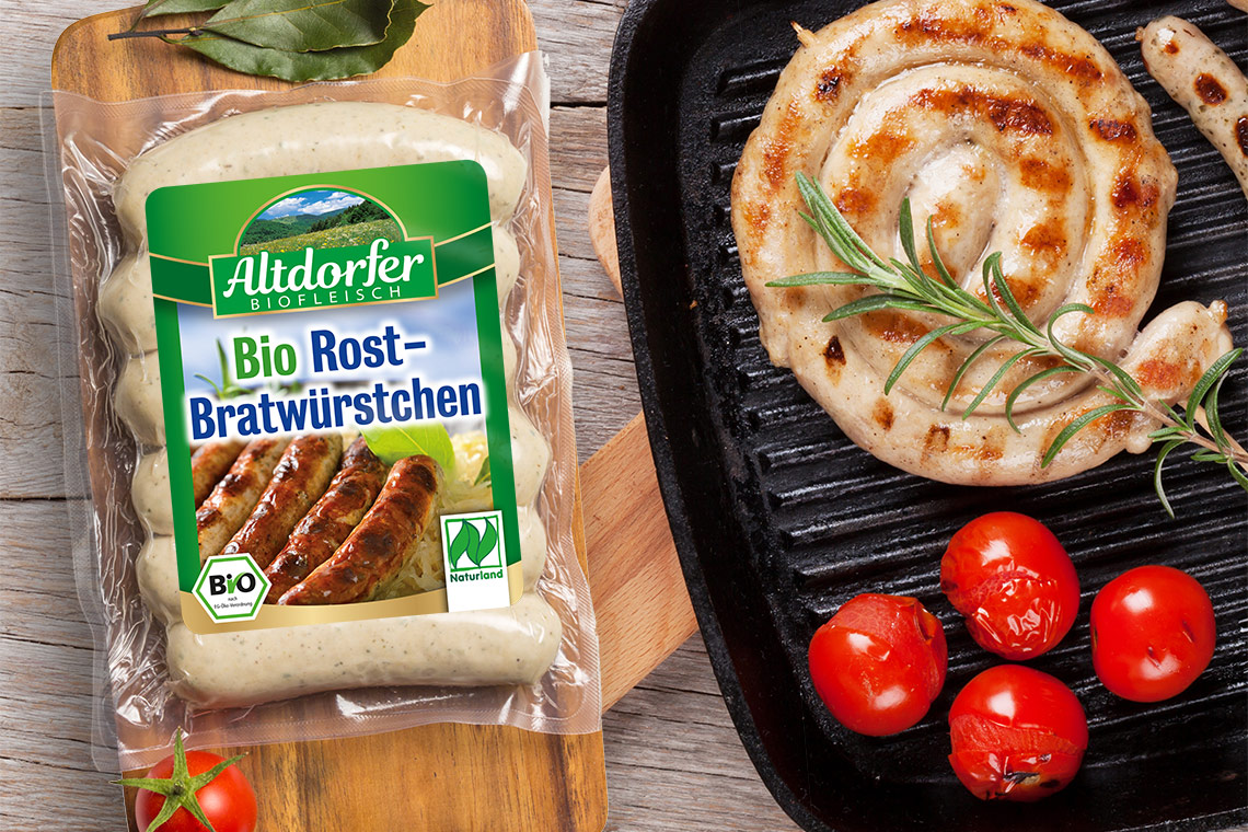 Packung Altdorfer Bio Rost-Bratwürstchen neben einer Bratwurstschnecke in der Grillpfanne