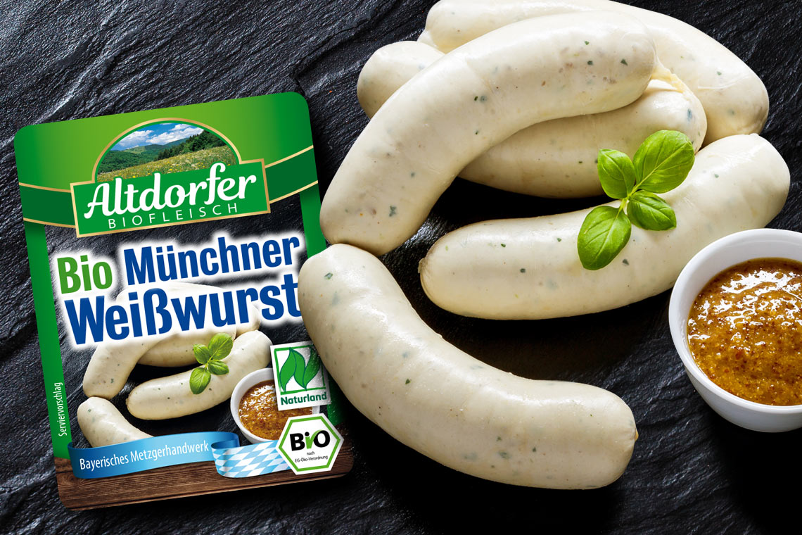 Packung Altdorfer Bio Münchner Weißwurst neben Weißwürsten und süßem Senf auf Schiefer