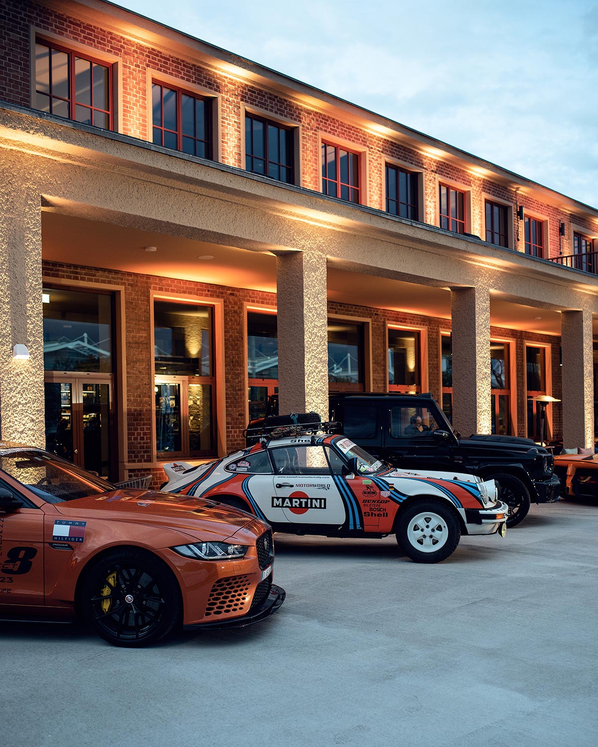 Renn- und Sportwagen vor dem beleuchteten Clubgebäude des Drivers & Business Club in der Dämmerung