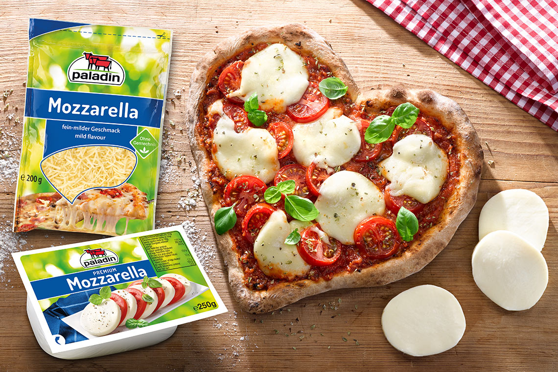 Herzförmige Pizza mit Mozzarella und Tomaten neben zwei Paladin-Mozzarella-Packungen