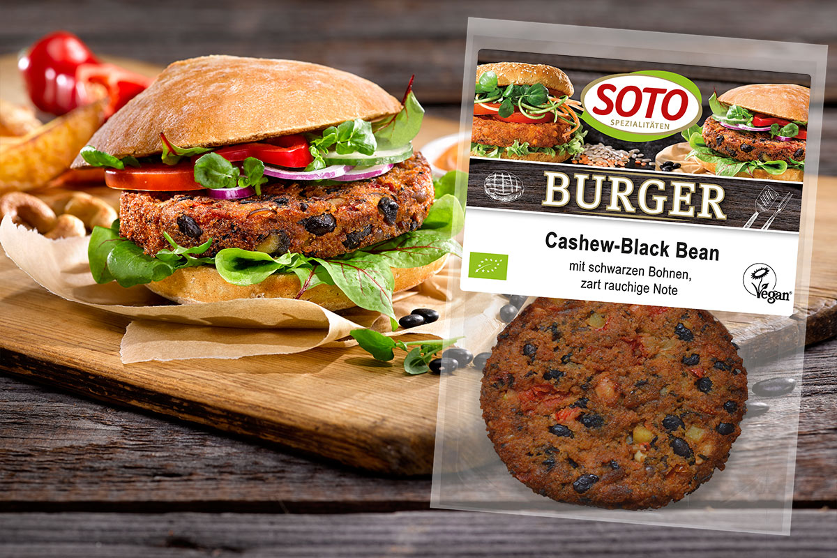 Packung SOTO Burger Cashew-Black Bean neben einem belegten Burger auf einem Holzbrett